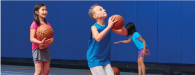 3 kids in multigym taking turns shooting basketball