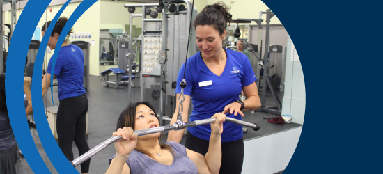 Female Mayfair Staff assisting member with lat pull-downs at Mayfair Parkway