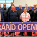 Image of Mayfair Staff standing on the new Pickleball Courts. There is a banner sign that says Grand Opening.