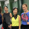 Image of female members at Mayfair West. They are holding pickleball paddles and they are standing on an indoor tennis court.