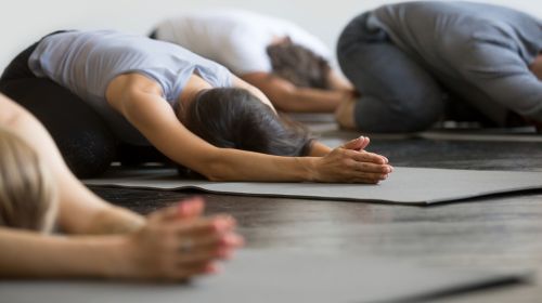 Stock image of some people in a child's pose while participating in a group exercise class.