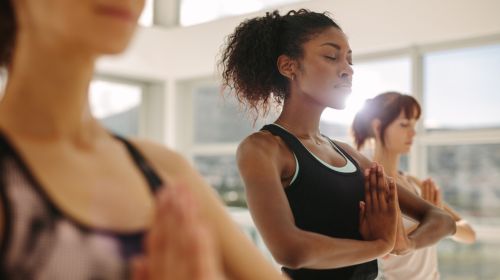 Stock image of women in a prayer or tree pose while participating in a yoga class.