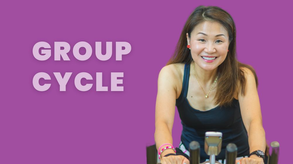 Asian women on an indoor bike smiling at the camera.
