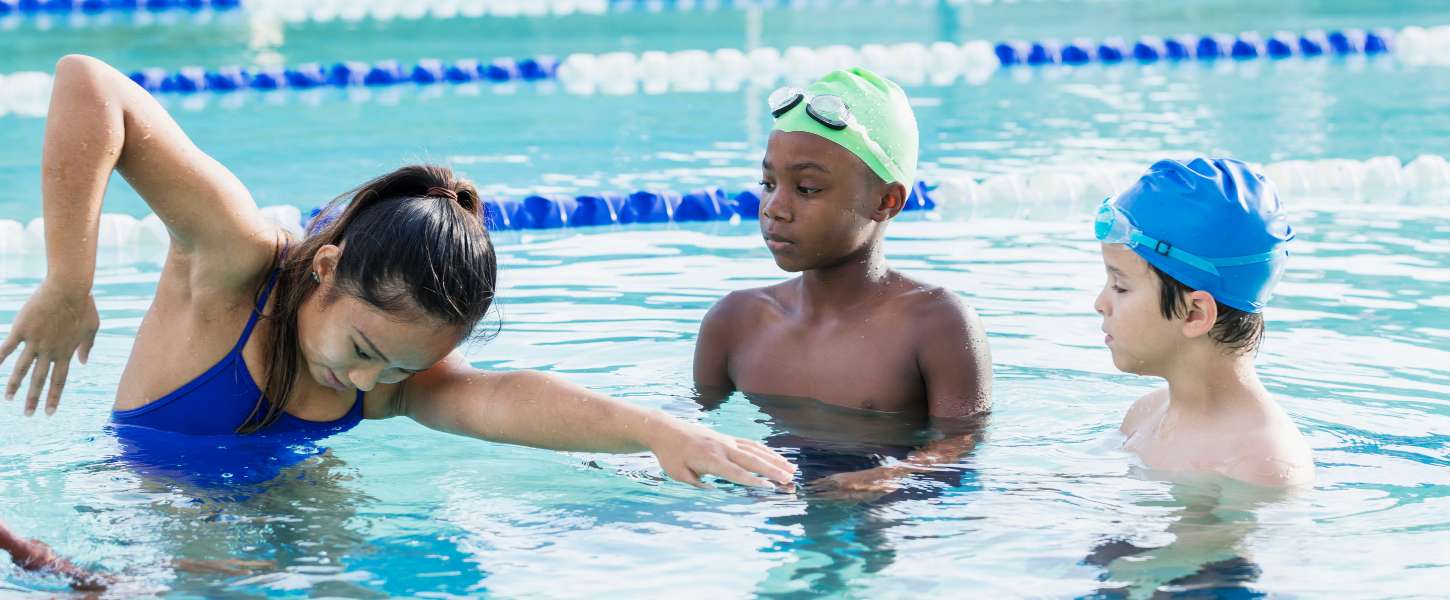 Image of female instructor showing front crawl technique to two young boys.