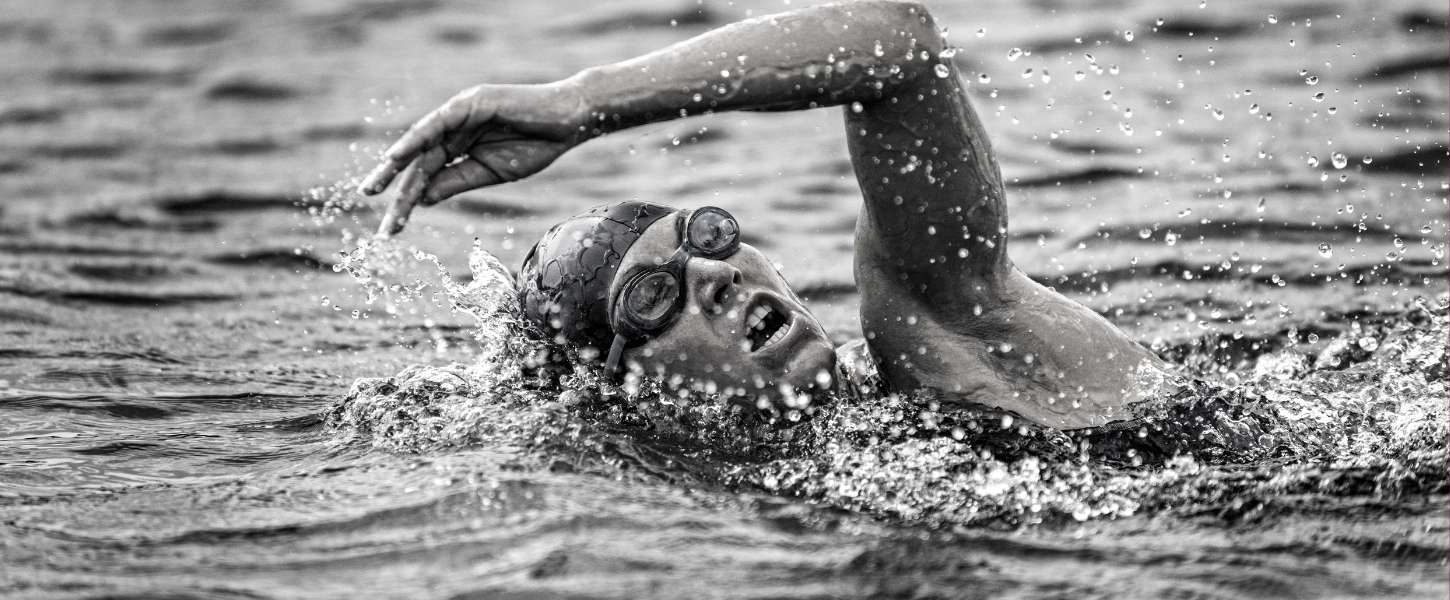 Black and white image of an adult female doing the front crawl in open water as part of a triathlon.