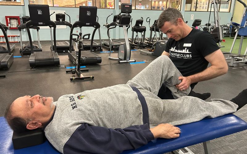 Image of personal trainer doing a muscle activation on an elderly male client on a stretching table in a gym. 