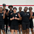 Image of a group of students wearing their team jerseys for the Squash Team they are on. They are on a Squash Court.